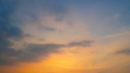 Obraz premium A serene sunset with the sky painted in soft hues of orange and yellow near the horizon. Dark clouds add depth and contrast to the warm tones, creating a peaceful ambiance. Sunset sky background. 