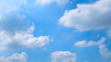 Obraz premium A serene blue sky filled with fluffy white clouds scattered across the expanse. The sunlight illuminates the scene, creating a peaceful and uplifting atmosphere. Nature's beauty background. 
