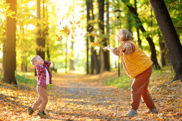 Mother and her son are having fun in the autumn park. A beautiful woman throws up yellow maple...