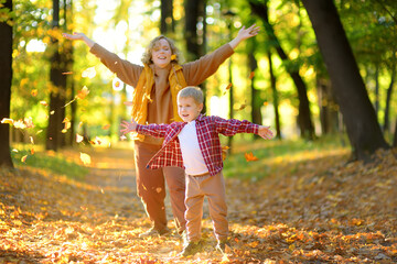 Mother and her son are having fun in the autumn park. A beautiful woman throws up yellow maple...