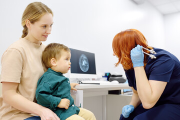 Baby and his mother are being seen by a pediatric neurologist in medical clinic. Doctor conducts tests, checks the reflexes, hearing of small patient using tuning fork. Highly qualified cure