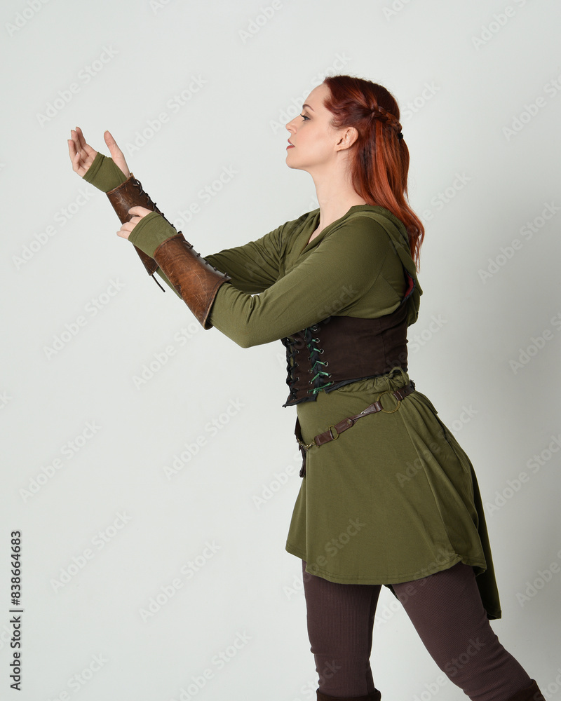 Canvas Prints Close up portrait of beautiful  red haired female model, wearing green and brown medieval fantasy costume with tunic and armour. Standing  with gestural hand poses, isolated on white studio background