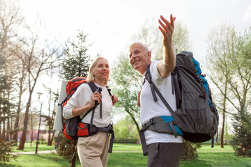 elderly athletic couple of seniors man and woman with hiking backpacks travel in the forest...