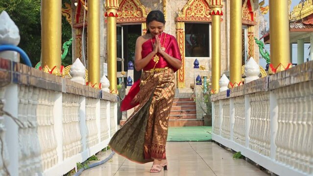 A young woman in a Thai dancer costume walks on a footbridge in a Buddhist temple and make thai greeting Wai