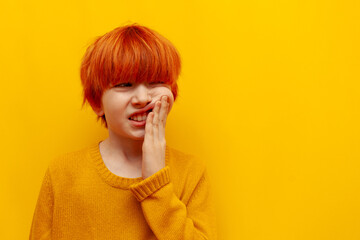 unhappy red-haired boy child suffers from toothache on yellow isolated background, sad teenager...