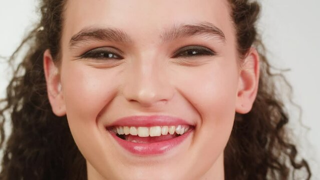 Young attractive brunette woman with curly hair looking and smiling at the camera close-up, Female with smoky eyes make-up. Makeup tutorial.