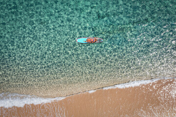 Aerial view of a woman on a surfboard in the turquoise waters of the Maldives