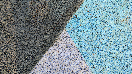 A close-up of a textured surface with sections of dark gray, light gray, and blue gravel creating...
