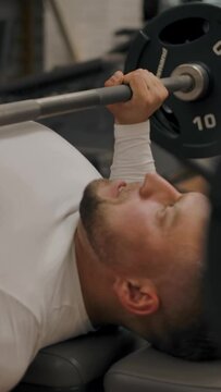 Powerful man does a bench press with a barbell. Muscular sports trainer conducts strength training in a modern gym. Vertical shot.