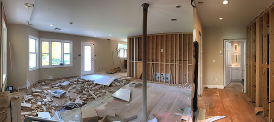 A construction worker is using a sledgehammer to demolish a wall, creating an open floor plan during a home renovation. Dust and debris cloud the air as the worker makes progress on the project.