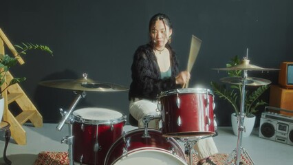 Professional Asian female drummer playing music on drum set while performing in studio. Zoom off shot