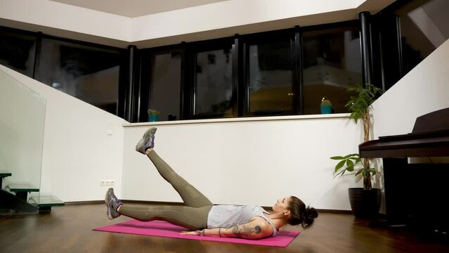 Raising her legs alternately, the woman is doing flutter kicks to strengthen her core and the muscles of her abdominal wall.