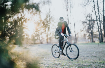 Obraz premium A man in casual wear rides his bicycle through a lush park, basking in the afternoon sun, embodying relaxation and a healthy lifestyle. Blurred photo.