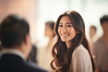 Fototapeta premium Dialogue unfolds as Asian woman, clad in white business attire, engages in conversation amid bustling public space backdrop, her demeanor poised and engaged.
