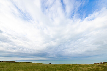 Scenic view of a wide, cloudy sky over a peaceful sea and grassy landscape in a serene, natural setting.