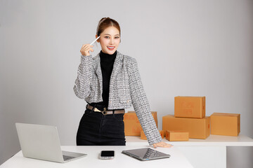 Asian smart entrepreneur business woman in casual suit surround by parcel boxes using computer...