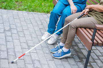 A nurse and an elderly blind woman are sitting on a bench in the park. Close up of legs. 
