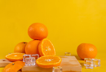 pile of oranges, ice cubes and cutting board isolated yellow background