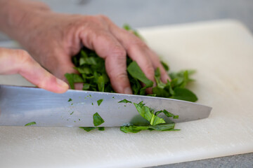 A cook slices fresh spinach leaves on a board with a knife.