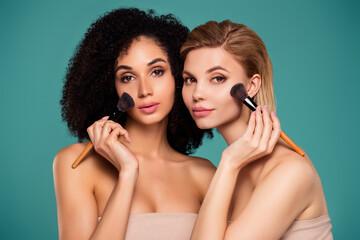 Photo of two attractive girls applying cosmetics on face with brush isolated cyan color background