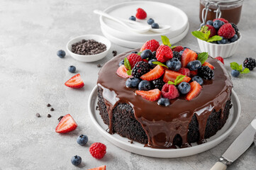 Delicious chocolate cake with chocolate glaze and fresh berries on a white plate on a gray concrete...