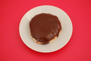 A chocolate covered doughnut on a white plate, tempting and delicious