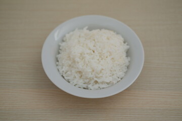 A bowl of white rice on a wooden table.