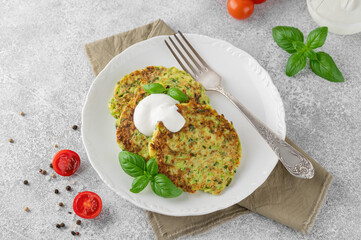 Zucchini fritters or zucchini pancakes on a white plate with fresh basil and sour cream. Top view, selective focus.