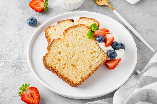 Delicious vanilla pound cake served with fresh berries and whipped cream on a gray concrete background. Selective focus, copy space.