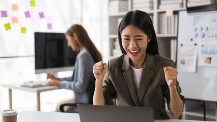 Businesswoman reading finance data on laptop and raising arm to celebrate with successful business