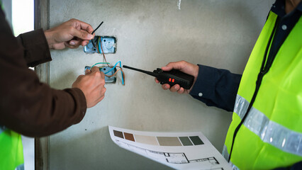 Two engineers holding blueprint and inspecting electrical system of building in construction site