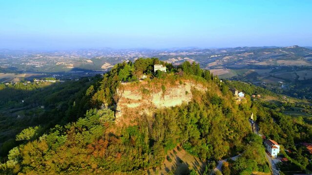 Pristine aerial pullback shot from Penna San Giovanni (MC), the highest precipice of the town surrounded by rich vegetation, punctuated buildings and the typical vast Marche expanses in the background