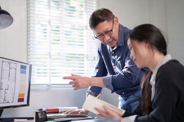 Interior designer women and senior businessman checking blueprint of construction architectural plan on computer while discussing and choosing color swatch samples of interior design of building