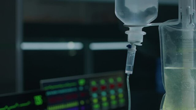 No people closeup of vital signs monitor showing heart rate and blood pressure of patient and iv drip bag with serum in dark operating room