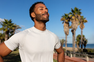 African American man breathing deeply in nature. Black man in sports clothing feeling good after exercising.