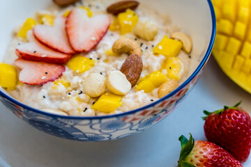 A bowl of oats with strawberries and mango arranged on a plate