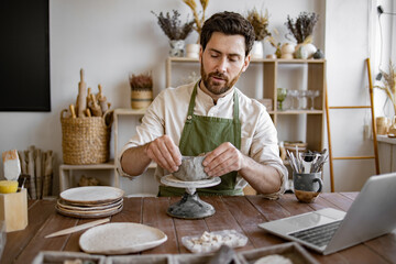 Male artist carefully shaping clay pot in rustic studio filled with pottery tools and materials....