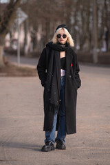 Portrait of a young beautiful blonde girl in a black coat outdoors in autumn.