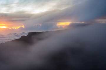 an ocean of clouds rolling over some rocky formations with the sun setting