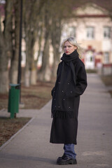 Obraz premium Portrait of a young beautiful blonde girl in a black coat outdoors in autumn.