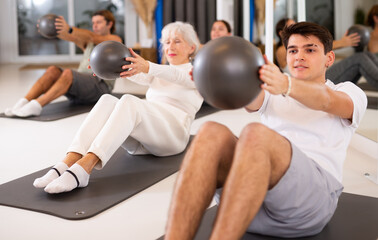 Slim young man practicing pilates with ball in training area during pilates classes