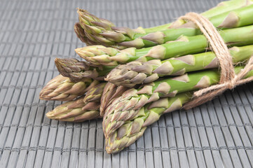 Fresh green asparagus spears neatly arranged on a bamboo mat, with natural lighting highlighting the vibrant green color.