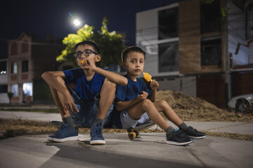 Obraz premium Boys eating popsicles while sitting on skateboard at night summer