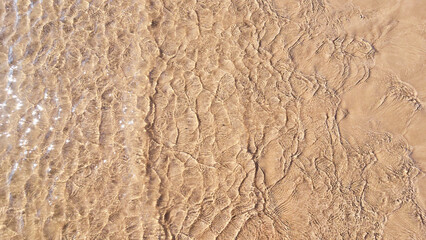 Small waves gently lap the sandy shore in this golden, textured beach pattern.