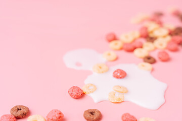 Breakfast cereals in the shape of rings with spilled milk on a pink background.