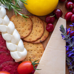 Cheese board for Jewish holiday Shavuot, for Harvest. Braided mozzarella, vegetable cookies, parmesan cheese, catmint flowers over wooden background.