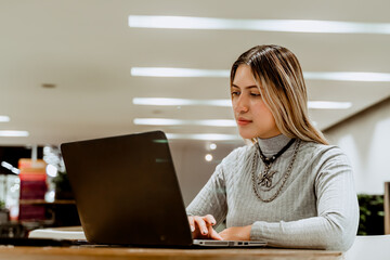 Fototapeta premium Empowered blonde-haired Latina woman working with her laptop at a coworker. Self-employed and entrepreneur. Financially independent.
