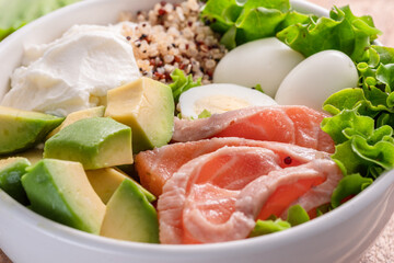 Salmon quinoa bowl with greens and vegetable on the wooden table. Balance in bowl. Top view.