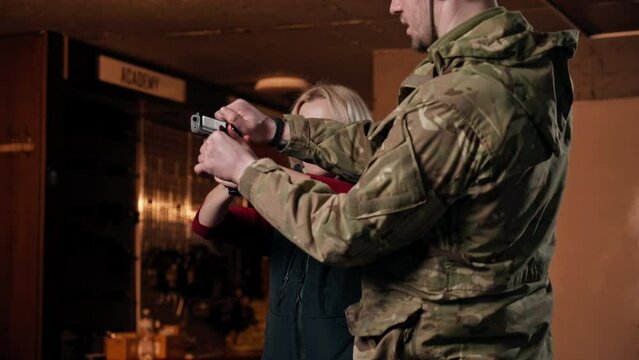 professional shooting range military man tells and shows a girl the correct stance with a pistol is