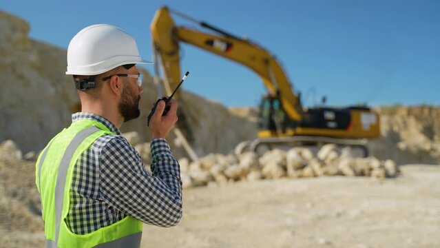 Engineer giving commands to employee in drilling machine using walkie talkie at quarry